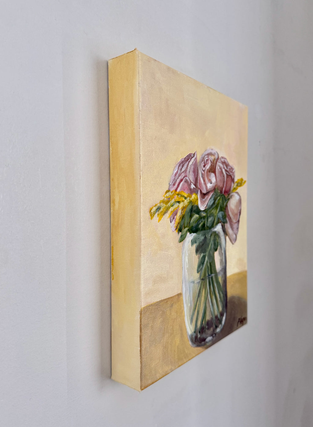 Acrylic painting of pink roses with greenery and yellow flowers in a glass vase on a yellow background. side view of painting.