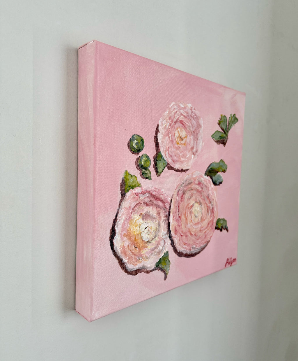 Painting of pink flowers with green leaves on a pink background. view of the side of the painting.